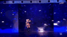 a female wrestler is walking on a stage in front of a screen that says live .
