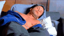 a shirtless man is laying on a couch with a blue towel on his chest