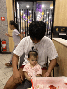 a man holding a baby wearing a white shirt that says lets