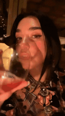 a woman in a plaid shirt is holding a glass of red liquid in her hand