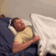 a man is laying in bed with a pillow and a blanket on his head .