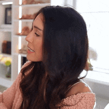 a woman with long dark hair is wearing a pink sweater and smiling