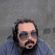a man with a beard and sunglasses is wearing headphones and a blue shirt .