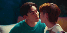 two young men are kissing each other on the forehead while sitting on a bed .