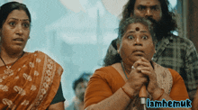 a woman with a surprised look on her face is next to a man and a sign that says iamhemuk