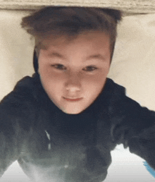 a young boy in a black shirt is laying on a bed looking up at the camera .