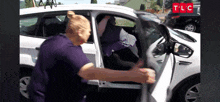 a woman in a purple shirt is getting out of a white car with tlc written on the bottom right