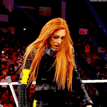 a woman with long red hair is wearing a black leather jacket and standing in a ring .
