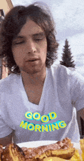 a man wearing a white shirt that says good morning is eating a plate of food