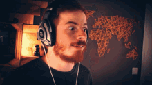 a man with a beard wearing headphones with a map of the world behind him