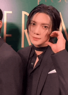 a man in a suit and choker is standing in front of a sign that says e on it
