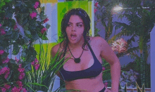 a woman in a bikini is standing in a garden with her mouth open and flowers in the background .