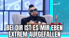 a man with a beard and sunglasses is sitting in a chair with a crown on it .