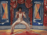 a man in a leotard and suspenders is dancing in front of a colorful curtain