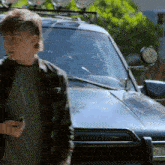 a boy in a plaid shirt stands in front of a car with a license plate that starts with t