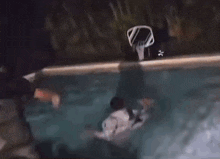 a person is falling into a swimming pool with a basketball hoop behind them