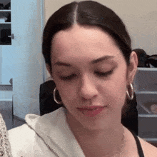 a woman wearing hoop earrings and a necklace is looking down at something .