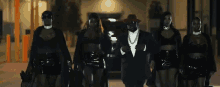 a man in a suit and hat is walking with three women .