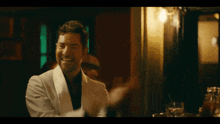 a man in a white suit is laughing while sitting at a table in a dark room .