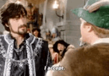 a man with a beard is talking to another man who is wearing a green hat and says i accept .