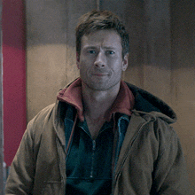 a man wearing a brown jacket with a red collar is smiling
