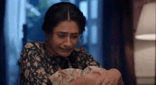 a woman is crying while holding a baby in her arms in a room .