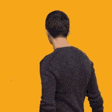 a man in a grey sweater is standing in front of a yellow background