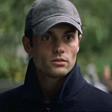 a man wearing a baseball cap and a black jacket looks at the camera