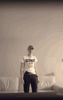 a man wearing a shirt that says schwand rot stands in front of a white couch