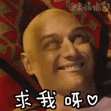 a bald man is smiling and laying on a bed with chinese writing on it .