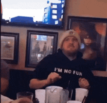 a man wearing a hoodie that says i 'm no fun is sitting at a table