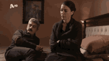 a man and a woman are sitting on a bed with a hd logo behind them