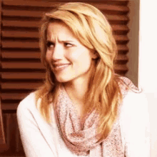 a woman wearing a scarf and a white sweater is making a face .