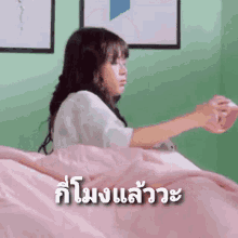 a girl is laying on a bed with a pink blanket and the words in a foreign language behind her