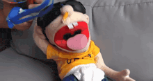 a puppet wearing a yellow shirt with the letter u on it is laying on a couch