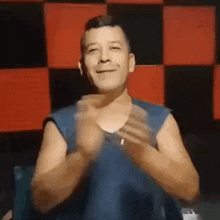 a man without a shirt is clapping his hands in front of a red and black checkered wall .