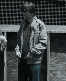 a man in a grey jacket is standing in front of a wooden wall
