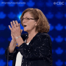 a woman wearing glasses and a sequined jacket applauds in front of a cbs logo