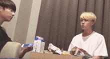 two young men are sitting at a table with a box of milk in front of them with chinese writing on it