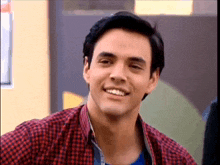 a man wearing a plaid shirt and a blue shirt smiles