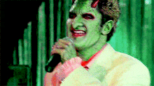 a man with green makeup is singing into a microphone