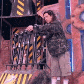 a man in a camouflage jacket is standing in front of a fence with a sign that says ' doritos ' on it