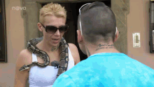 a woman with a snake around her neck is talking to a man with a tattoo that says nova