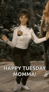 a woman is dancing on a wooden floor with the words `` happy tuesday momma '' written on it .