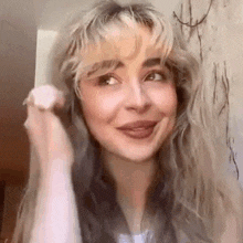 a close up of a woman 's face with blonde hair and bangs smiling .