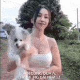 a woman in a white tank top is holding a small white dog in her arms
