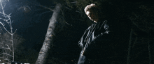 a man in a black jacket is standing in the dark in front of a tree