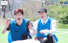two boys wearing blue nike vests are laughing on a field