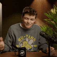 a man wearing a wu-tang sweatshirt sits at a table