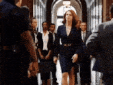 a woman in a blue suit is walking down a hallway surrounded by people in suits and ties .